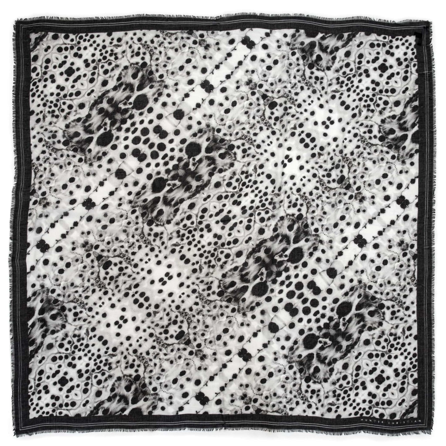Flat lay of the Hemera scarf by Hunter Christian, featuring sheer black and white inkblot patterns with a dark border and hand-frayed fringe, made in Italy from modal and silk.